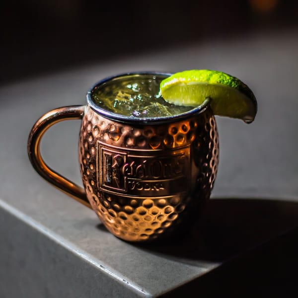 A copper Moscow Mule mug with a drink, ice, and a lime wedge on a dark surface.