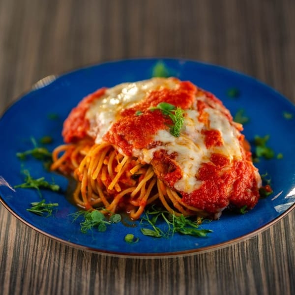 Spaghetti with red sauce and melted cheese, garnished with fresh herbs on a blue plate.