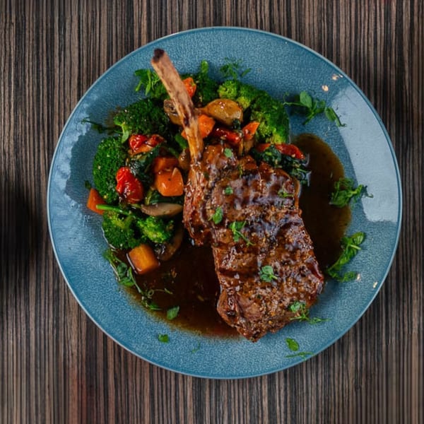 A Flavio Restaurant DC steak with bone, broccoli, and roasted vegetables on a blue plate.