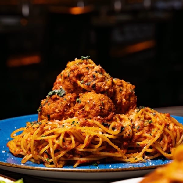 Spaghetti with large meatballs, red sauce, and herbs on a blue plate at Flavio Restaurant DC.