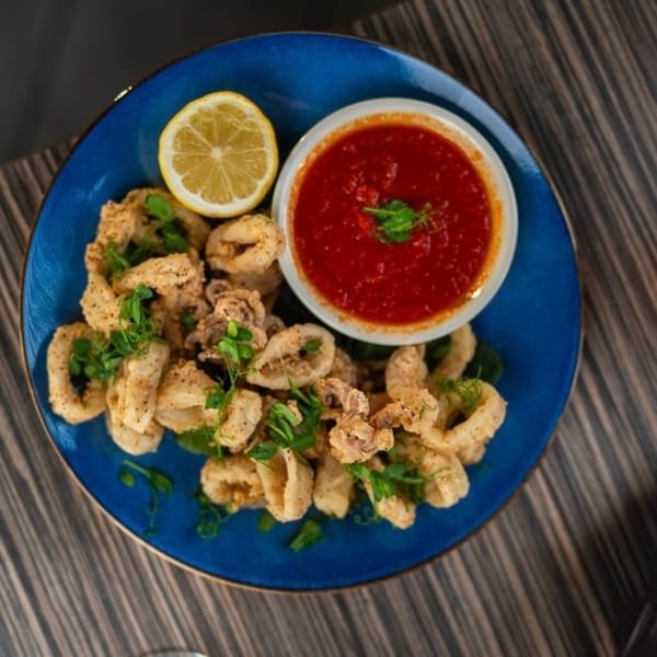 Flavio Restaurant DC's fried calamari with marinara sauce and a lemon wedge on a blue plate.