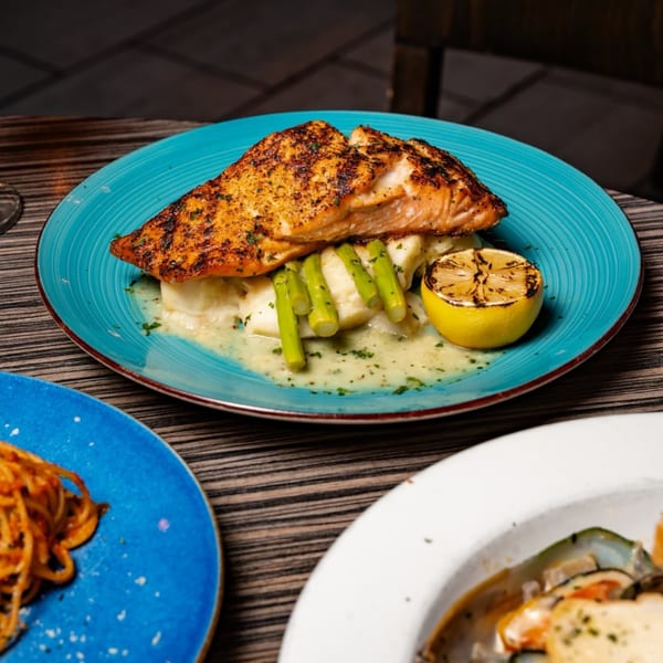 Grilled salmon with asparagus, mashed potatoes, and a lemon half on a blue plate at Flavio Restaurant DC.