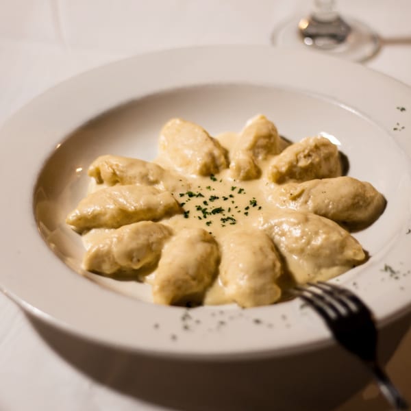 Flavio Restaurant DC's Italian gnocchi in a creamy sauce, garnished with herbs on a white plate.