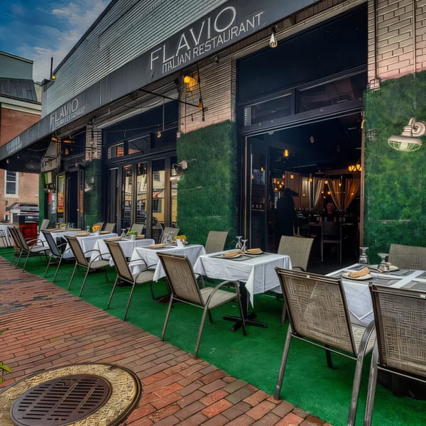 Flavio Italian Restaurant's outdoor patio with tables, chairs, and green turf, next to a brick sidewalk.