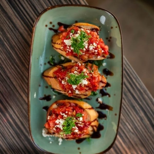 Three bruschetta appetizers with diced tomatoes, feta, and greens on a teal plate.