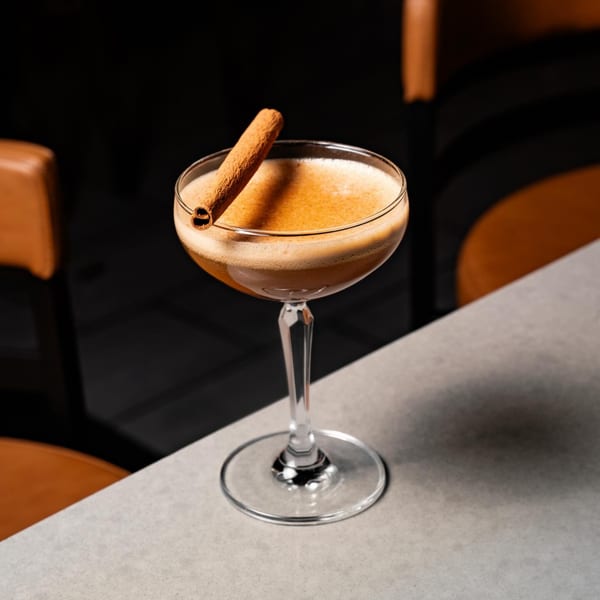 A Flavio Restaurant DC cocktail, garnished with a cinnamon stick, sits on a light gray table.