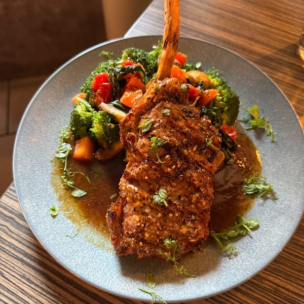 A large bone-in steak with roasted broccoli and cherry tomatoes on a gray plate.