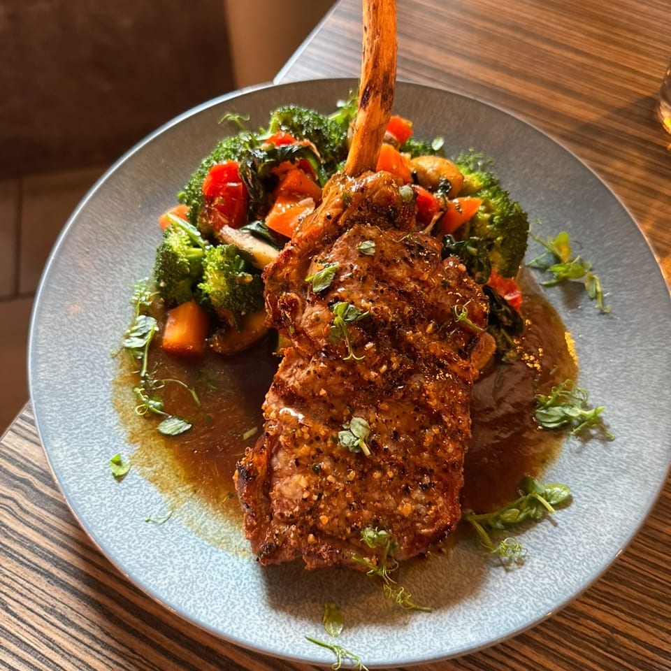 A large bone-in steak with roasted broccoli and cherry tomatoes on a gray plate.