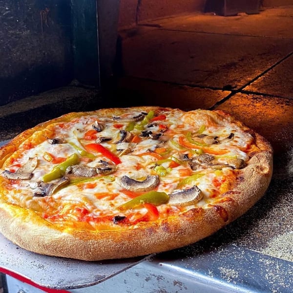 Freshly baked Flavio Restaurant DC pizza with mushrooms, peppers, and melted cheese on a peel.