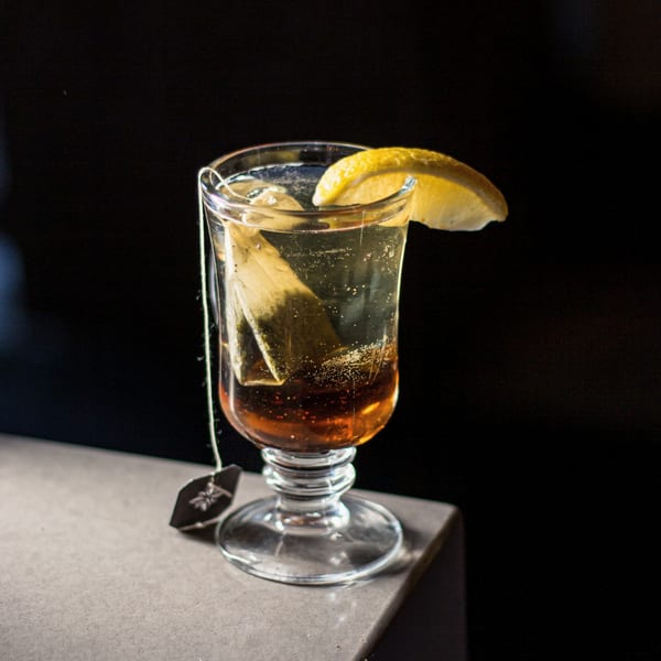 A tall glass of iced tea with a lemon slice and tea bag, on a gray surface.
