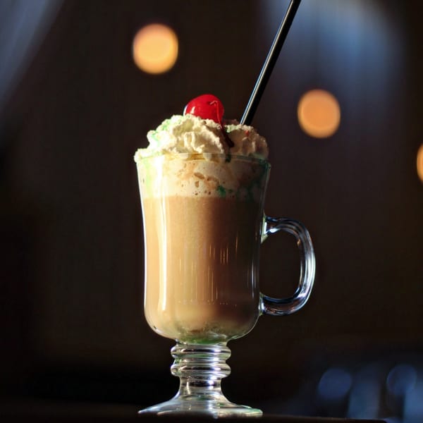 A Flavio Restaurant DC Irish coffee with whipped cream, a cherry, and a black straw.